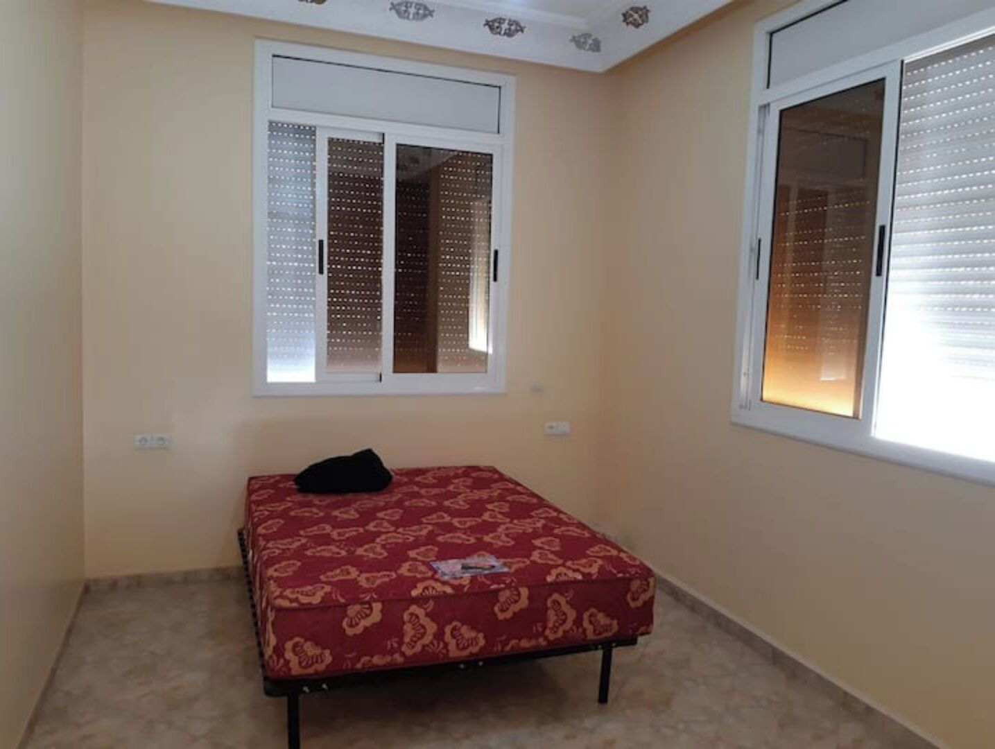 Une chambre à coucher avec un lit, deux fenêtres équipées de stores et une couvre-lit à motifs.