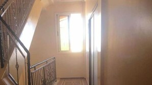 A hallway with a patterned floor, a staircase with a metal railing, and a window allowing natural light. - Family apartment in Tagadirte! (Agadir)