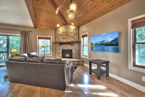 A living room with a stone fireplace, a leather sofa, and a large window with a mountain view. - Central to World-Class Resorts - Private Hot Tub Managed by Park City Lodging (Park City)