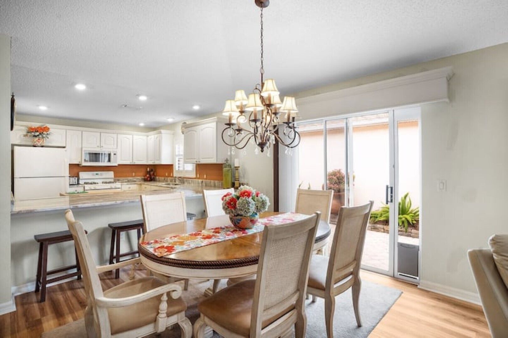 A spacious kitchen with white cabinets, a dining area with a wooden table and chairs, and a chandelier.