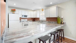 Una cocina moderna con armarios blancos, una isla grande con taburetes de bar, microondas, estufa y lavaplatos.