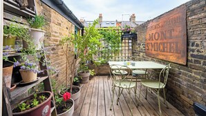 A wooden deck with a table and chairs, surrounded by potted plants and a rustic brick wall. - The Mad Hatter (London)