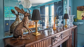 A wooden console table with decorative items, a mirror reflecting the room, and a window with curtains. - The Mad Hatter (London)
