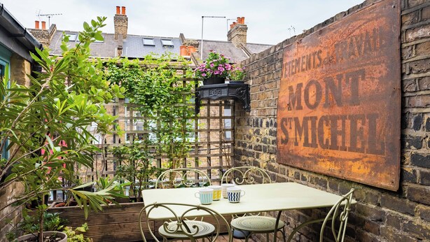 A rustic outdoor seating area with a metal table and chairs, surrounded by potted plants and a brick wall. - The Mad Hatter (London)