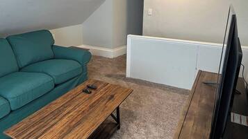 Um quarto pequeno e acolhedor, com um sofá azul-esverdeado, uma mesa de centro de madeira e uma televisão.