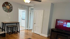 A living room with a wooden floor, a TV, a fireplace, and a dining area with a table and chairs. - Main, Three Bedroom House in Historic Loveland (Loveland)