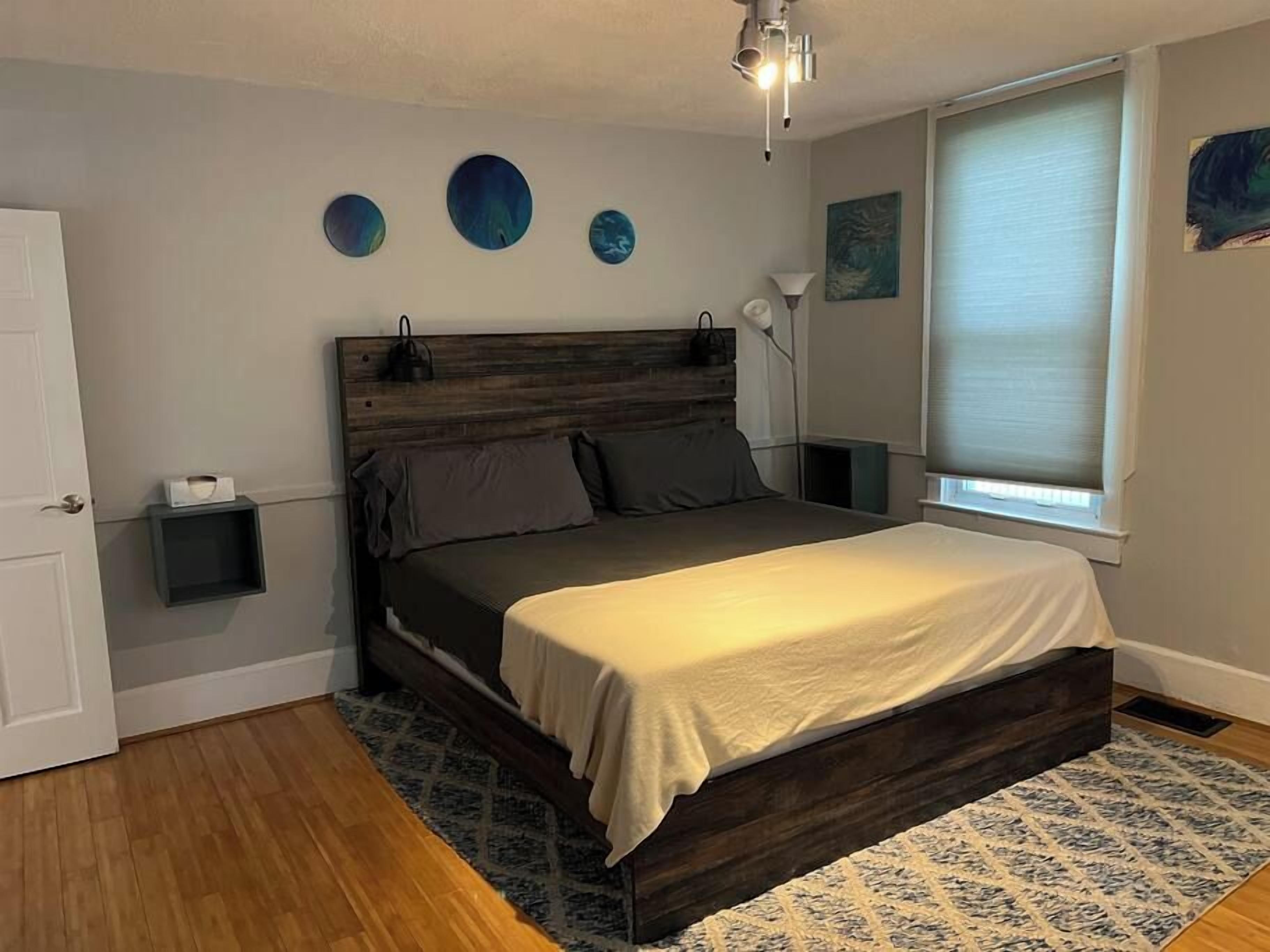 Un dormitorio con estructura de cama de madera, una mesita de noche y una lámpara de pared.