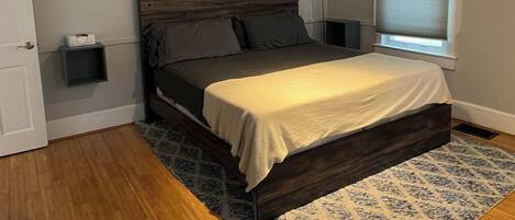 Un dormitorio con estructura de cama de madera, una mesita de noche y una lámpara de pared.