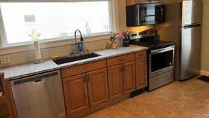 A kitchen with wooden cabinets, stainless steel appliances, a microwave, a refrigerator, and a window with blinds. - Main, Three Bedroom House in Historic Loveland (Loveland)