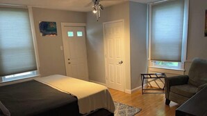 Een slaapkamer met een bed, een stoel, een plafondventilator en twee ramen met jaloezieën.