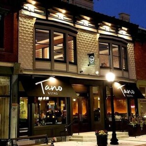 Un edificio con dos escaparates, uno de los cuales muestra el rótulo iluminado "Tano BISTRO".