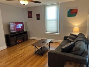 Una sala de estar con televisor, piso de madera, un sofá, una mesa de centro y chimenea.
