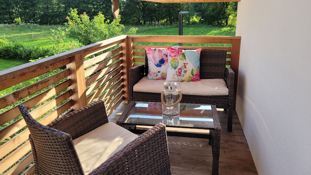 Area relax esterna coperta, con mobili in vimini e un tavolo in vetro, affacciata su un paesaggio verdeggiante.