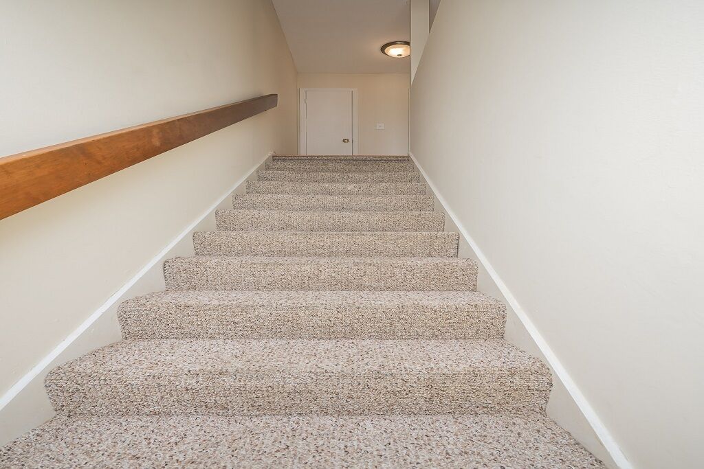 A carpeted staircase with a wooden handrail, leading to a white door at the top.