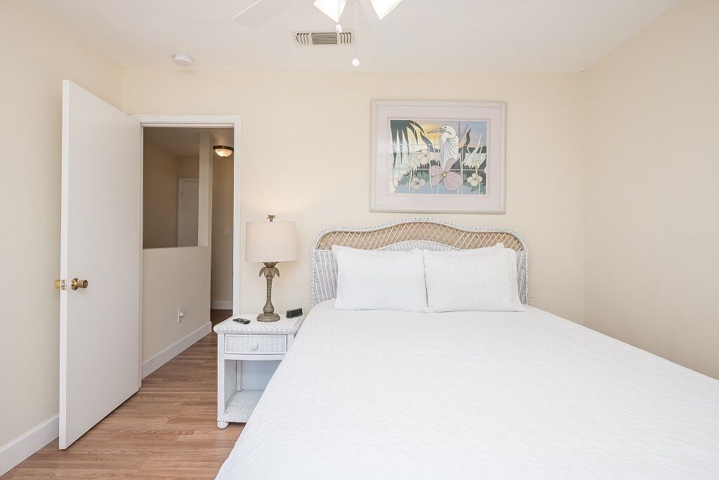 Un dormitorio con cama, mesita de noche, lámpara y puerta que da a otra habitación.
