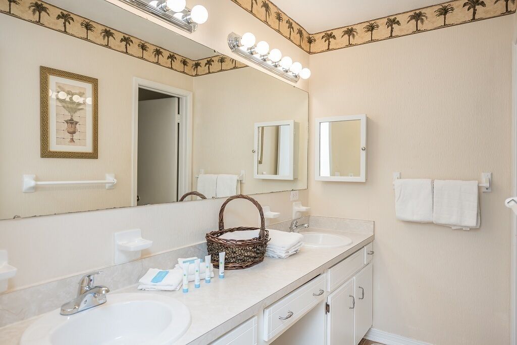 A bathroom with two sinks, a large mirror, and a vanity with a basket and towels.