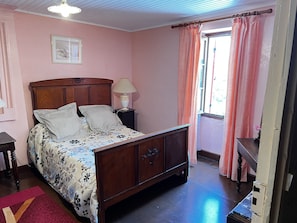 Une chambre à coucher avec un lit en bois, une table de chevet avec une lampe, une commode et une fenêtre avec des rideaux.