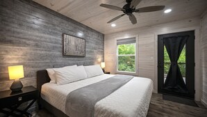 A bedroom with a bed, nightstands, a ceiling fan, a window, and a door leading to an outdoor area. - Forest Retreat Hot Tub Slide Arcade Family Fun (Broken Bow)