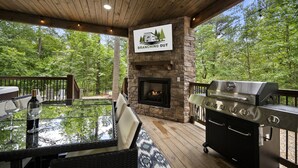 An outdoor patio with a stone fireplace, a grill, and a glass table with chairs. - Forest Retreat Hot Tub Slide Arcade Family Fun (Broken Bow)