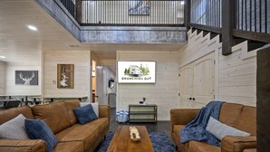 A modern living room with two brown leather sofas, a wooden coffee table, and a blue patterned rug. A sign on the wall reads "BRANCHING OUT." - Forest Retreat Hot Tub Slide Arcade Family Fun (Broken Bow)