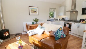 A cozy living room with a brown leather sofa, a wooden coffee table with a bottle of wine and glasses, a framed picture on the wall, and a kitchen in the background. - Rising Sun (York)