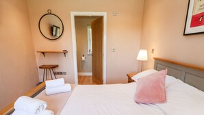 A hotel room with a bed, a bedside table with a lamp, a small stool, a towel rack, and a door leading to a bathroom. - Rising Sun (York)
