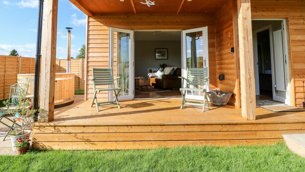 A wooden cabin with a covered patio, two chairs, and a dining table. - Rising Sun (York)