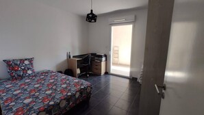 A bedroom with a bed, a desk, and a chair. There is a door leading to a balcony.