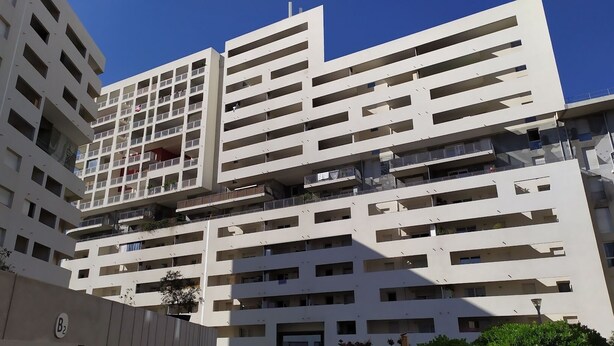 A multi-story residential building with balconies, a clear sky, and a visible sign with the letter 'B' and a number.