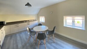 Una habitación amplia con cocina, una mesa de comedor con cuatro sillas y dos ventanas que aportan luz natural.