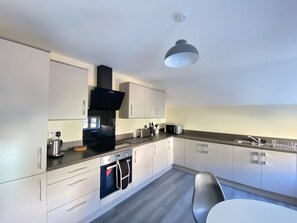 Een moderne keuken met witte kasten, een zwarte afzuigkap, een inbouwoven, een magnetron en een roestvrijstalen spoelbak.