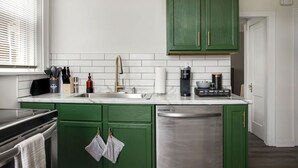 Una cocina con gabinetes verdes, un lavavajillas de acero inoxidable y un salpicadero de azulejos blancos.