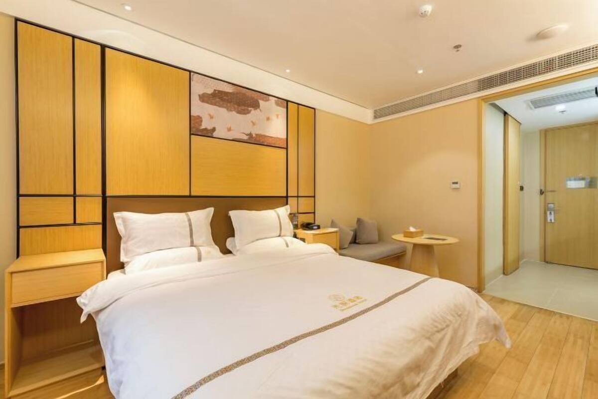 Habitación de hotel con una cama grande, un cabecero de madera, una mesita de noche pequeña y una obra de arte colgada en la pared.