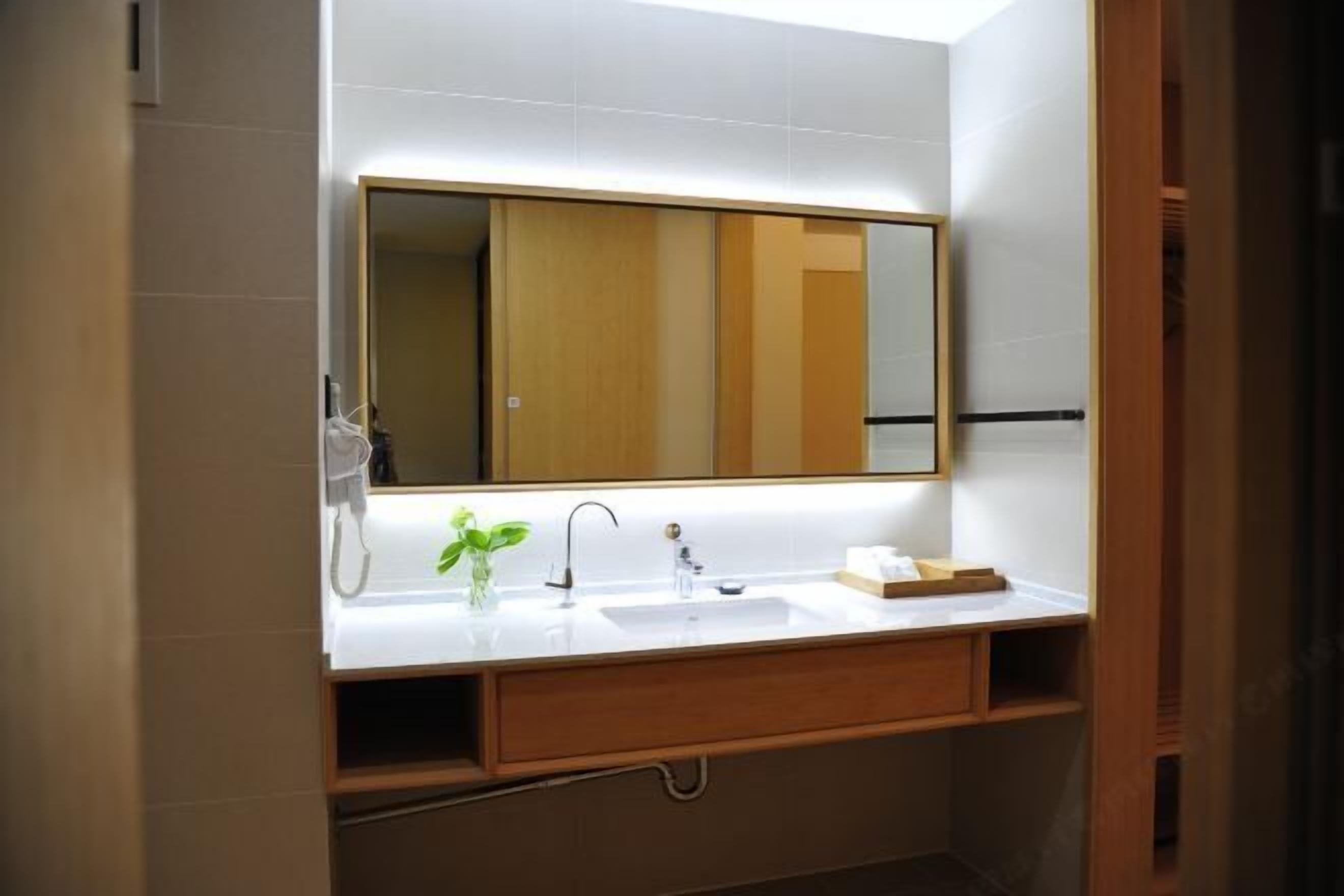 A modern bathroom with a large mirror, white sink, and wooden vanity.