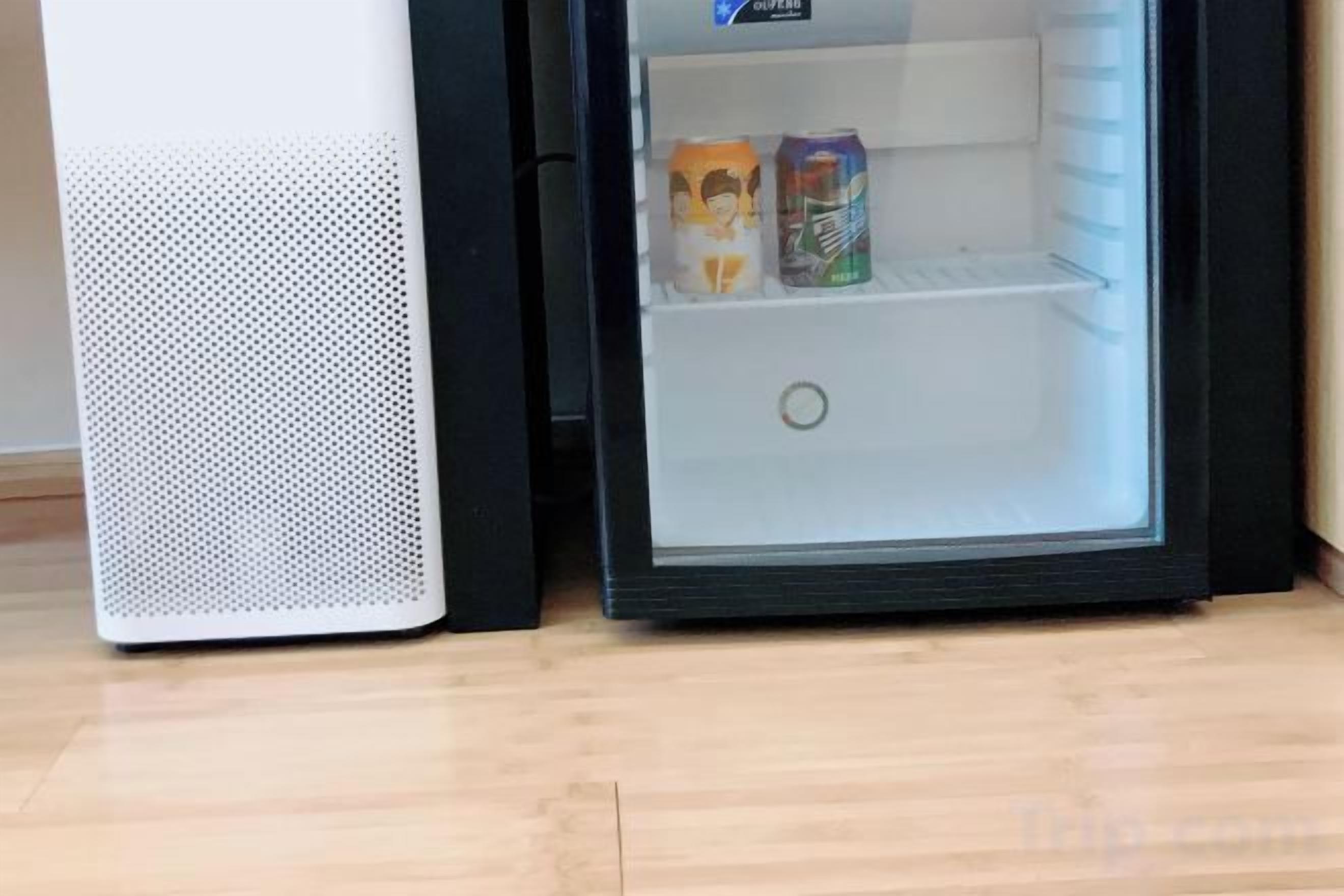 Un refrigerador negro con puerta de vidrio, que contiene algunas latas y una botella.