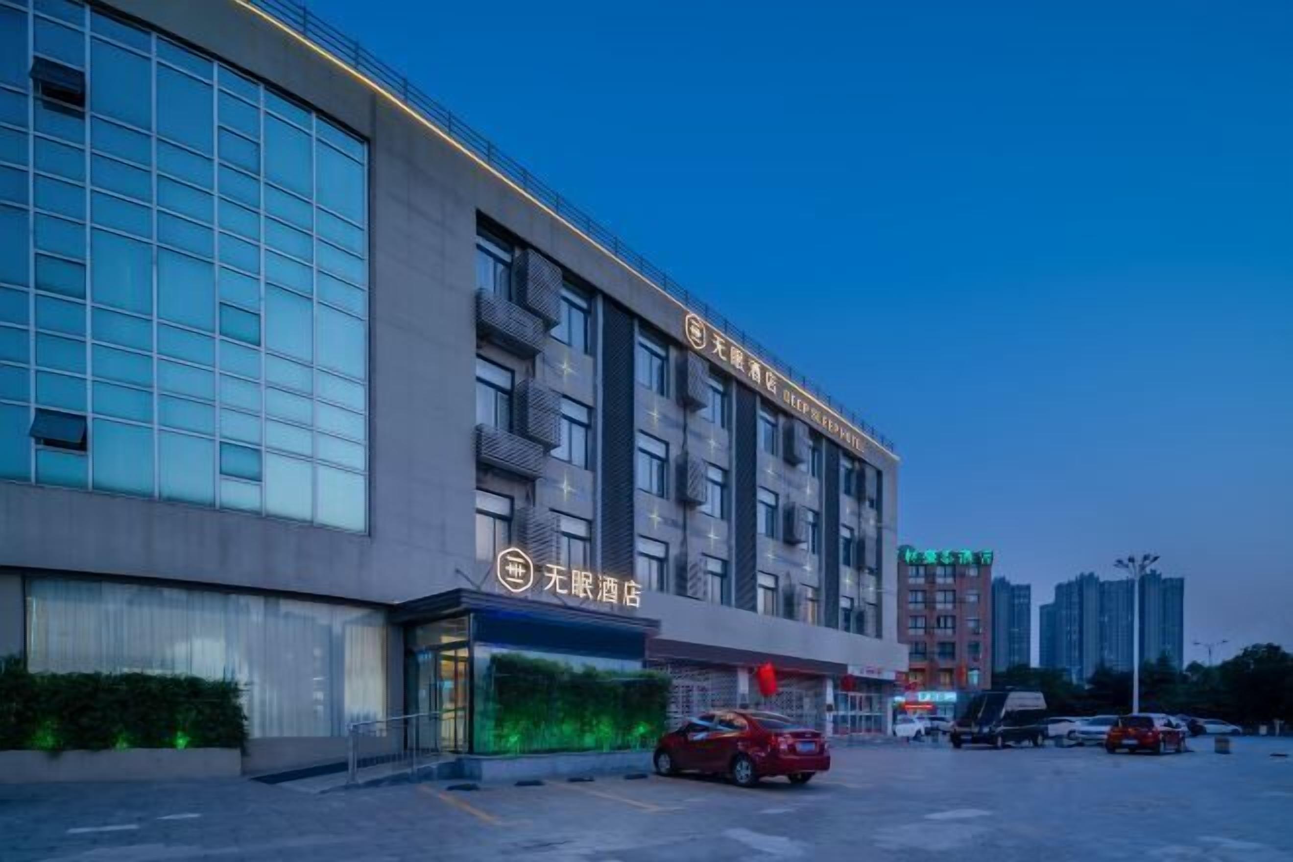 A modern hotel building with multiple floors, large windows, and a parking lot with several cars.