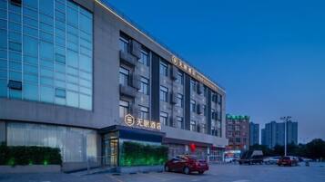 A modern hotel building with multiple floors, large windows, and a parking lot with several cars.