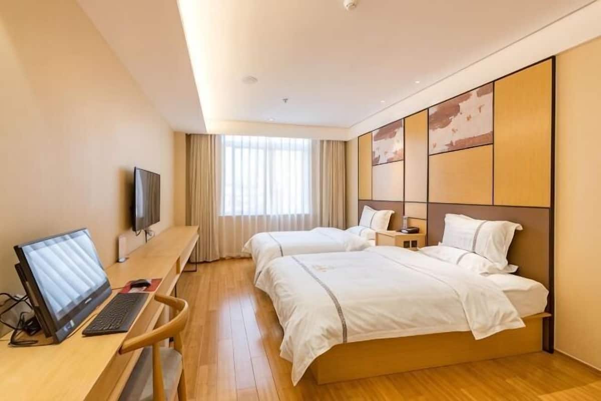 Habitación de hotel con dos camas, un escritorio con computadora, televisión y un amplio ventanal con cortinas.