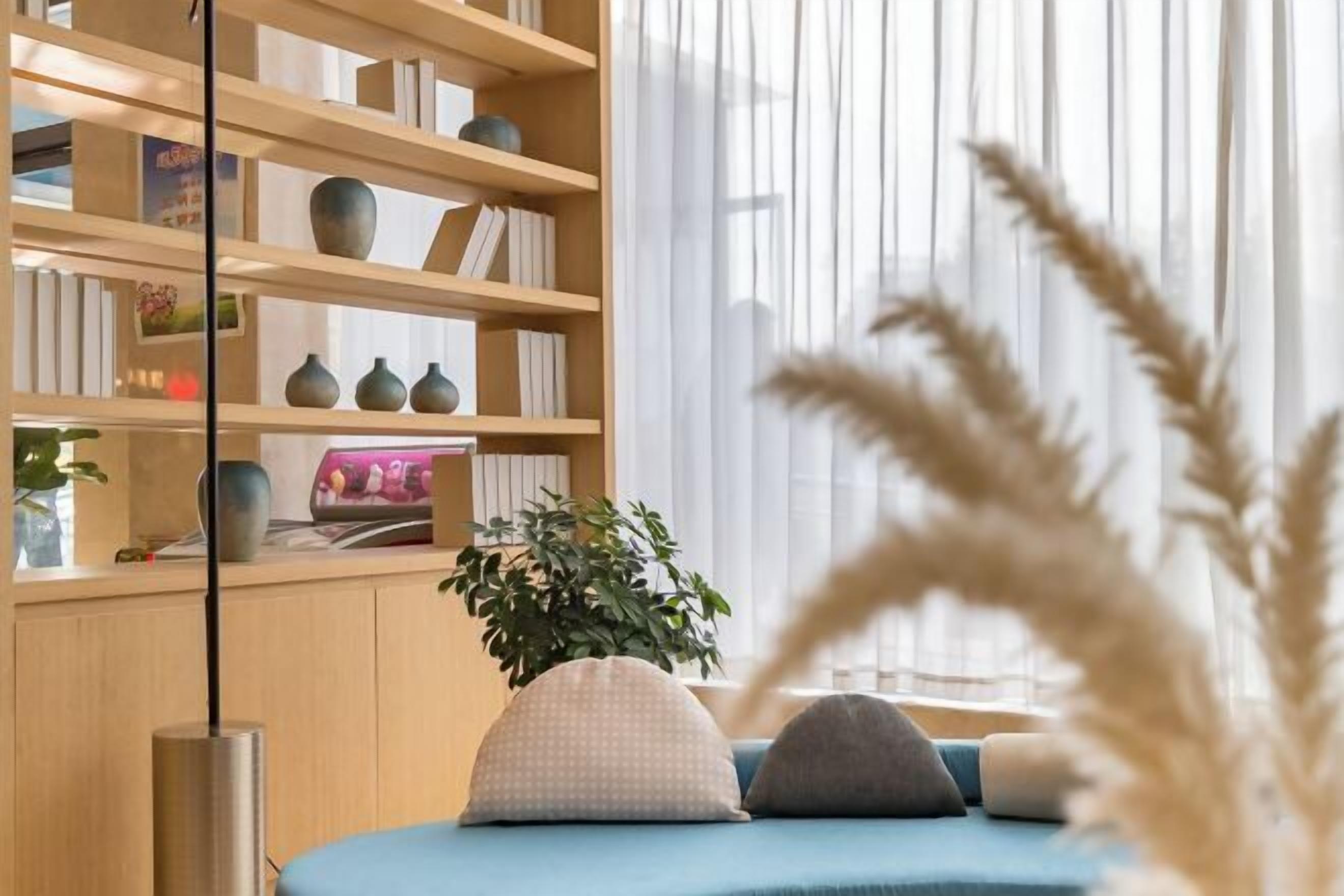 Ein modernes Wohnzimmer mit einem blauen Sofa, einem Holzregal und einem großen Fenster mit durchsichtigen Vorhängen.