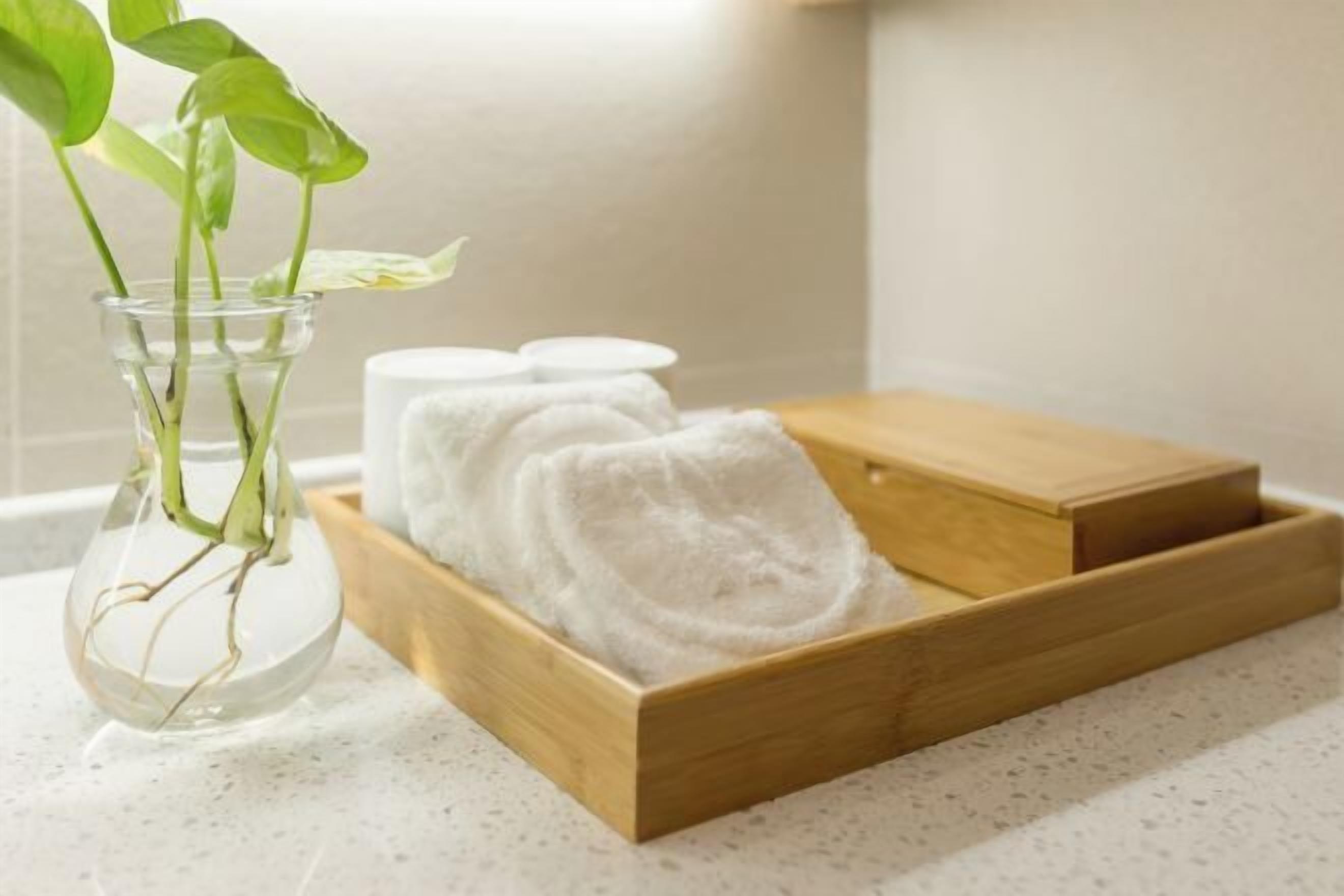 A clear glass vase with a plant and a wooden tray with folded towels.