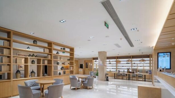 A modern interior with wooden shelving displaying various items, a central seating area with tables and chairs, and a reception desk. - Deep Sleep Hotel (Xuzhou High-Speed Railway Station Front Square Zhenxing Avenue) (Xuzhou)
