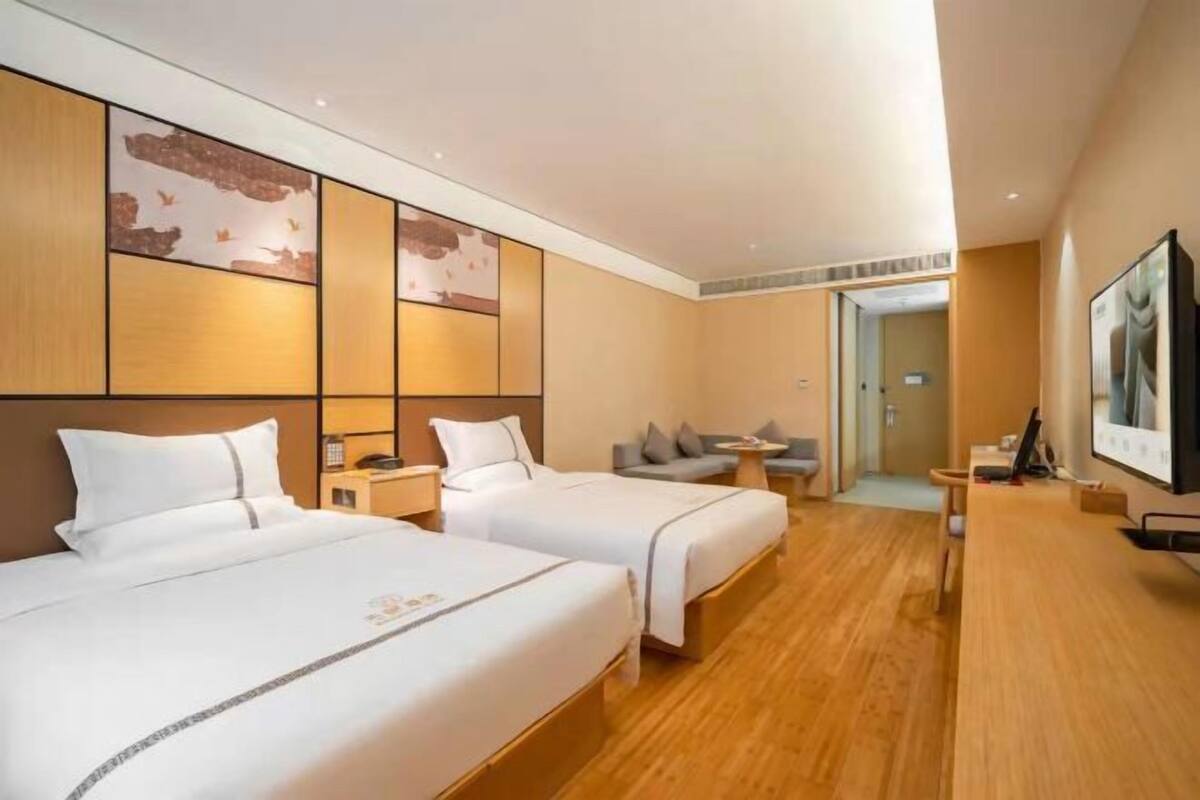Habitación de hotel con dos camas, un escritorio y un televisor. En la esquina, hay un sofá y una mesita.