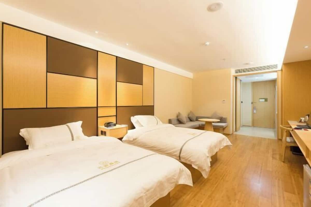 Habitación de hotel con dos camas, un sofá pequeño, un escritorio y una puerta que da a un baño.
