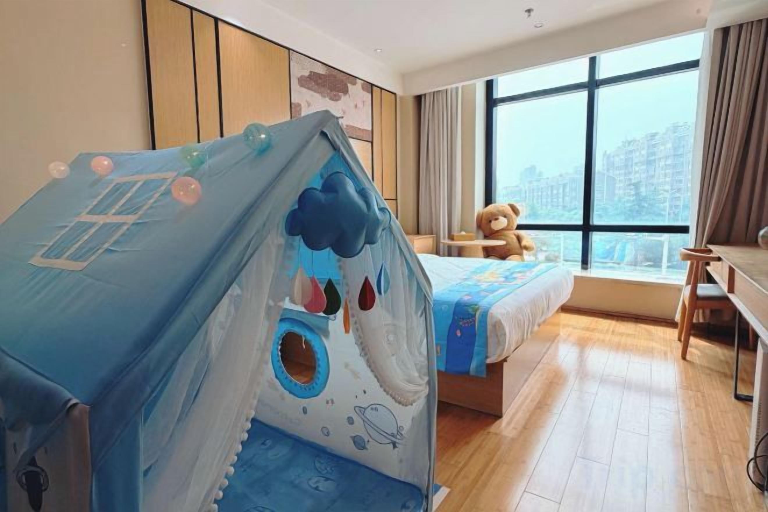 Ein Hotelzimmer mit einem Bett, einem Spielzelt, einem Teddybären und Blick auf die Stadt.