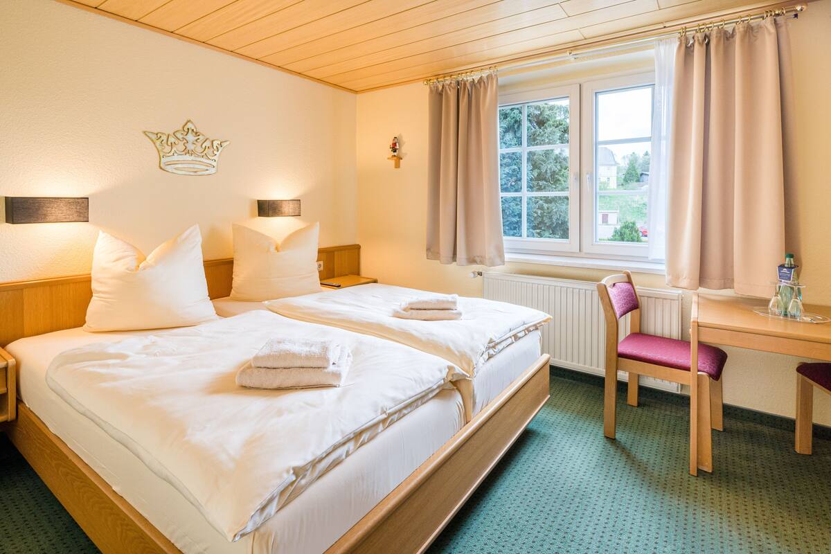 A hotel room with a large bed, two bedside tables, a desk with a chair, and a window with curtains.