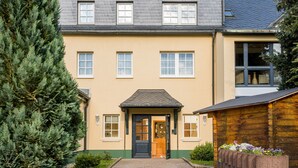 A two-story building with a beige facade, a dark roof, and a wooden structure to the right. - Landhaus Purschenstein (Neuhausen)