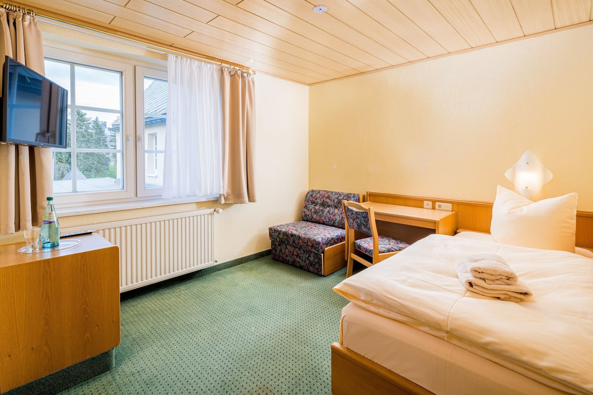 A hotel room with a bed, a chair, a desk with a television, and a window with curtains.