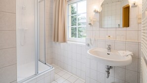 A modern bathroom with a glass shower enclosure, a sink with a mirror, and a window providing natural light. - Landhaus Purschenstein (Neuhausen)