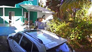 Une voiture est garée devant une maison à la façade verte et au toit recouvert de tuiles.
