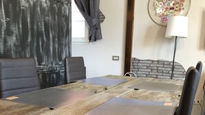 Een rustieke eettafel met een houten blad, omringd door zwarte stoelen. Achtergrond toont een bakstenen muur en een lijst met reisspeldjes.